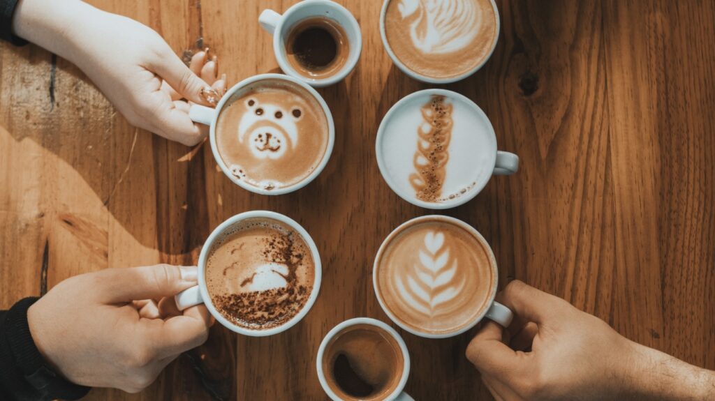 różne kawy na stole, filiżanki latte, espresso, cappucinno trzymane w rękach